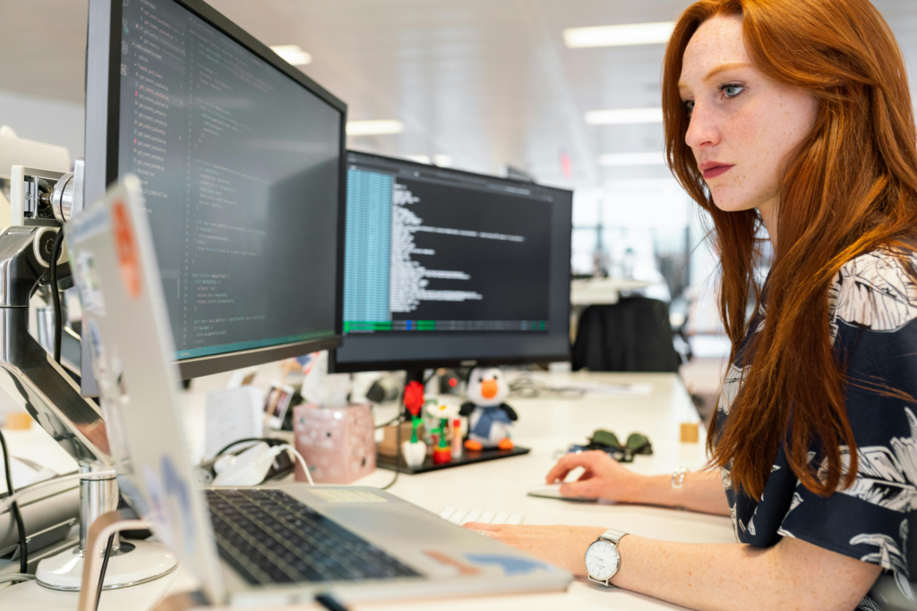 Woman at desk with laptop and two monitors