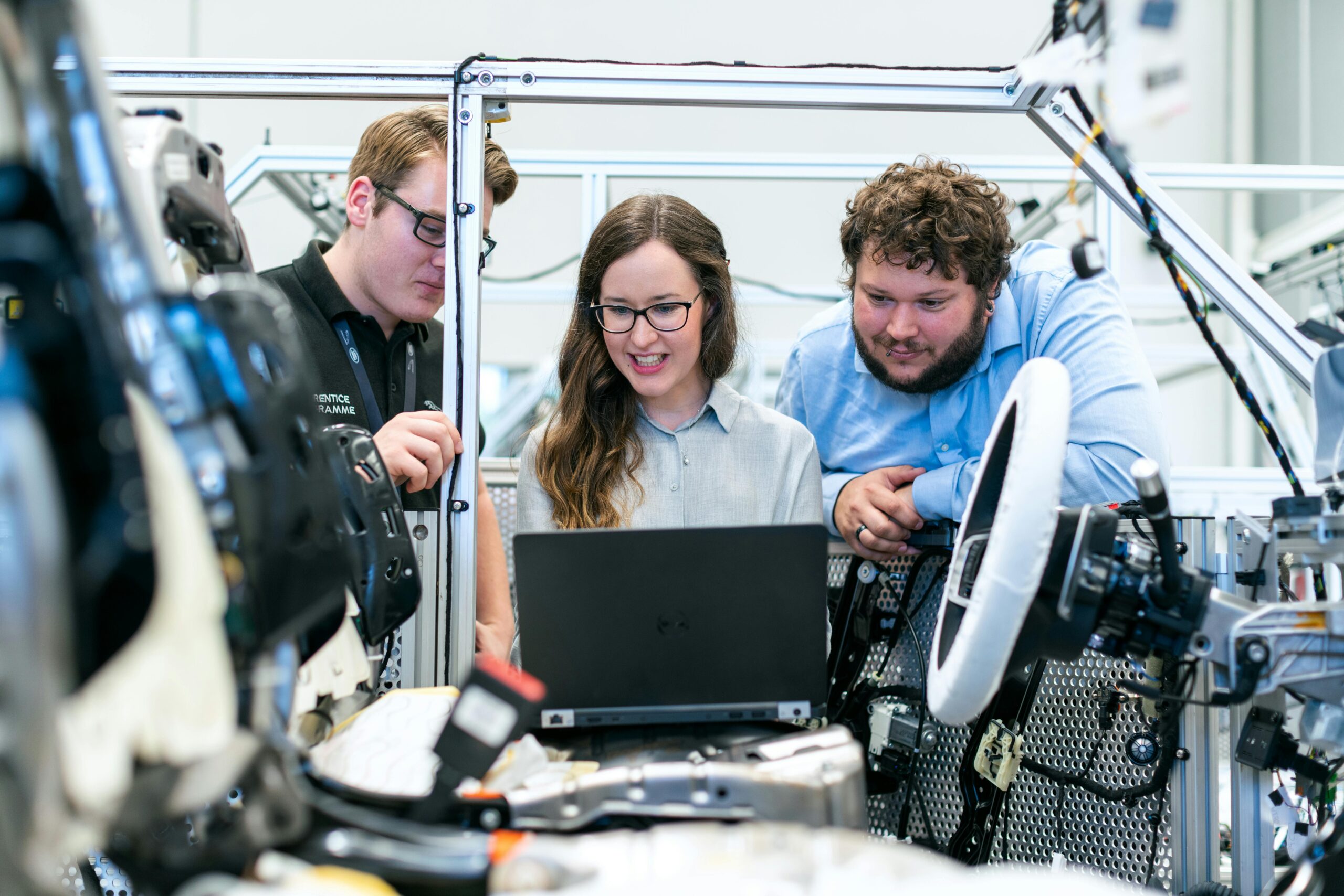 three employees in a car manufacturing plant looking at a screen on a laptop.