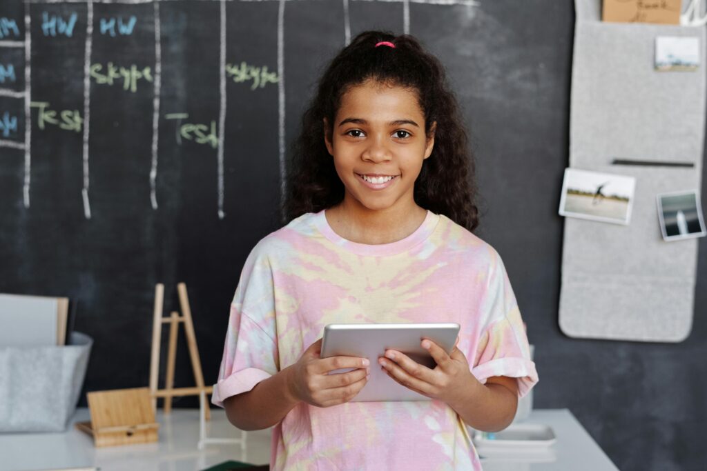 Girl holding a tablet in front of a blackboard in a classroom