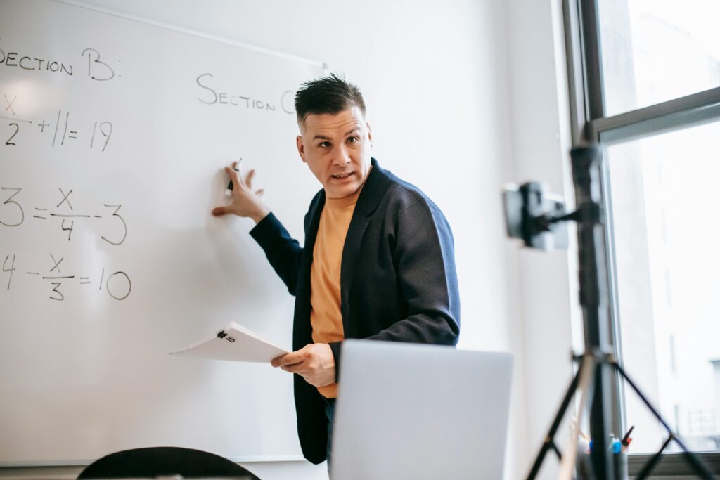 Photo of a man in front of a whiteboard teaching via smartphone