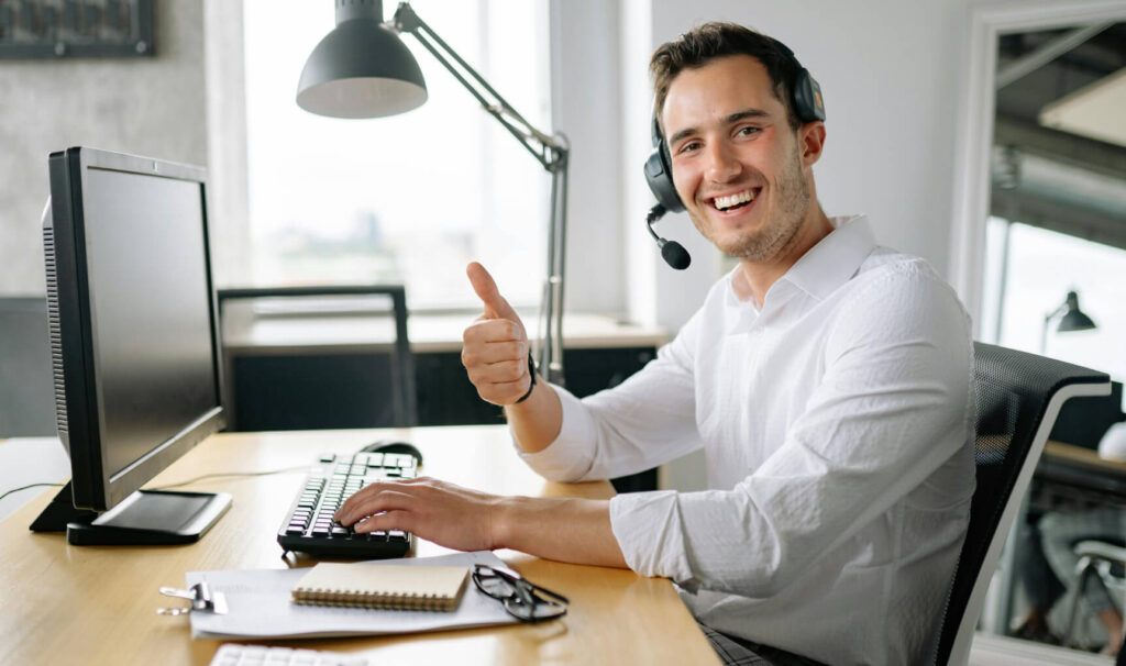 Person at a workstation wearing a headset and microphone giving the thumbs up