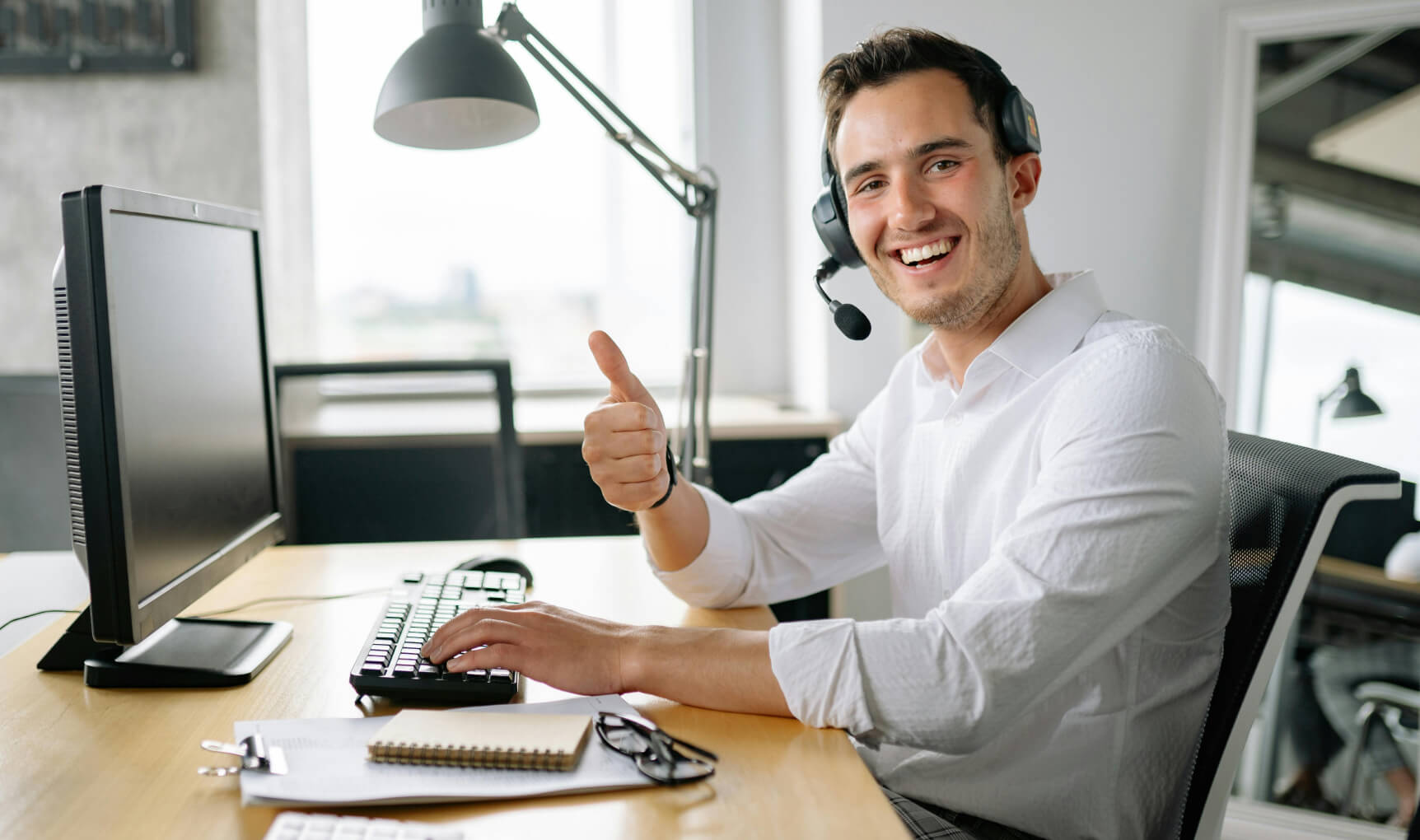 Person at a workstation wearing a headset and microphone giving the thumbs up