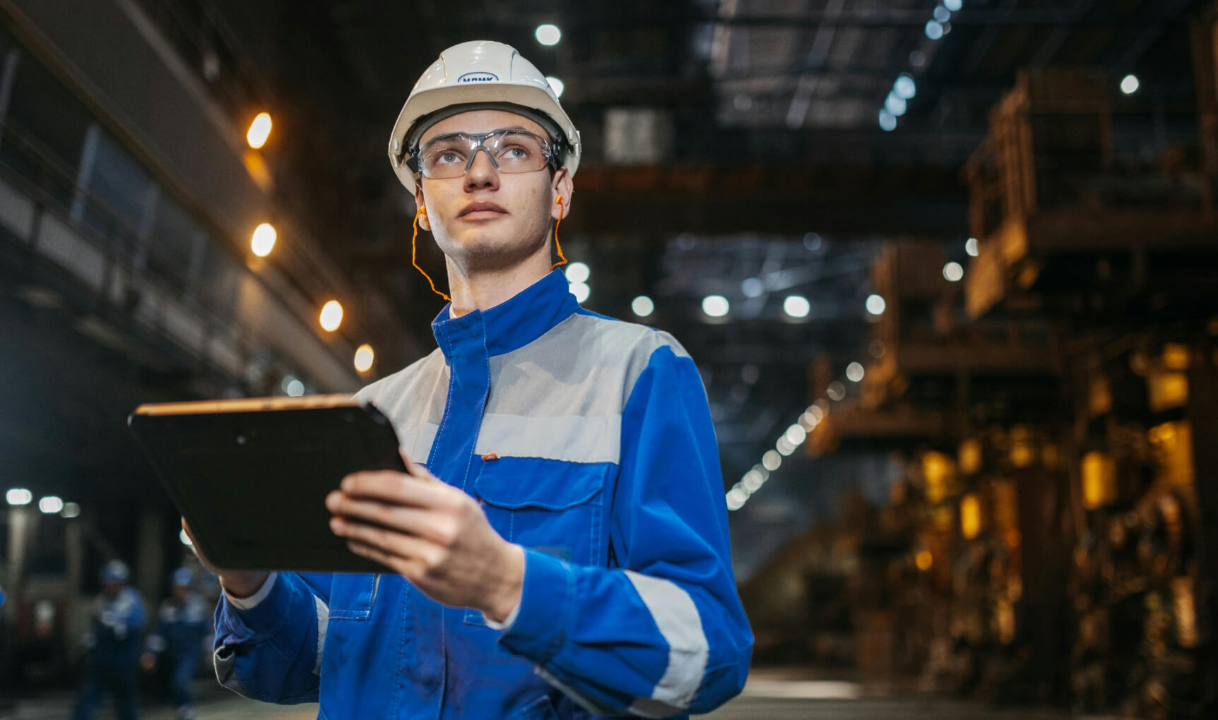Person standing in an industrial facility holding a tablet device