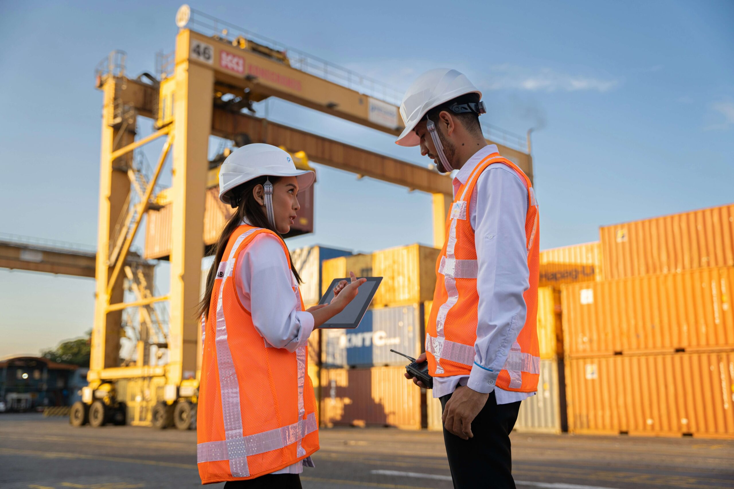 Two workers in high-vis clothing working with a tablet near shipping containers