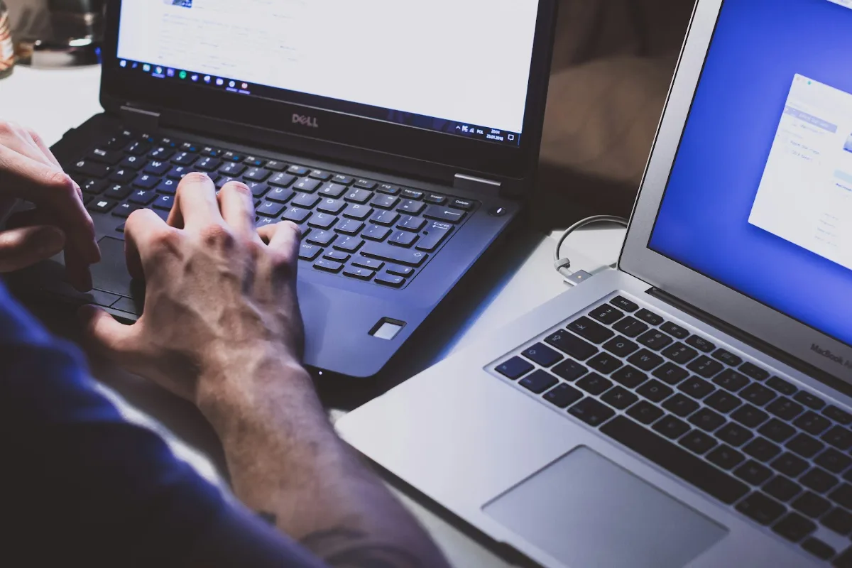 Person typing on a laptop next to a second laptop