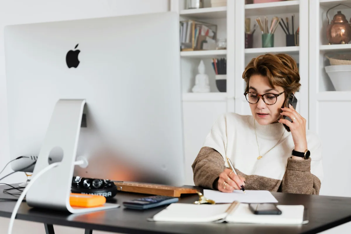 Woman taking notes during a phone call while working at an iMac