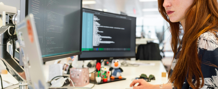 Woman at desk with laptop and two monitors